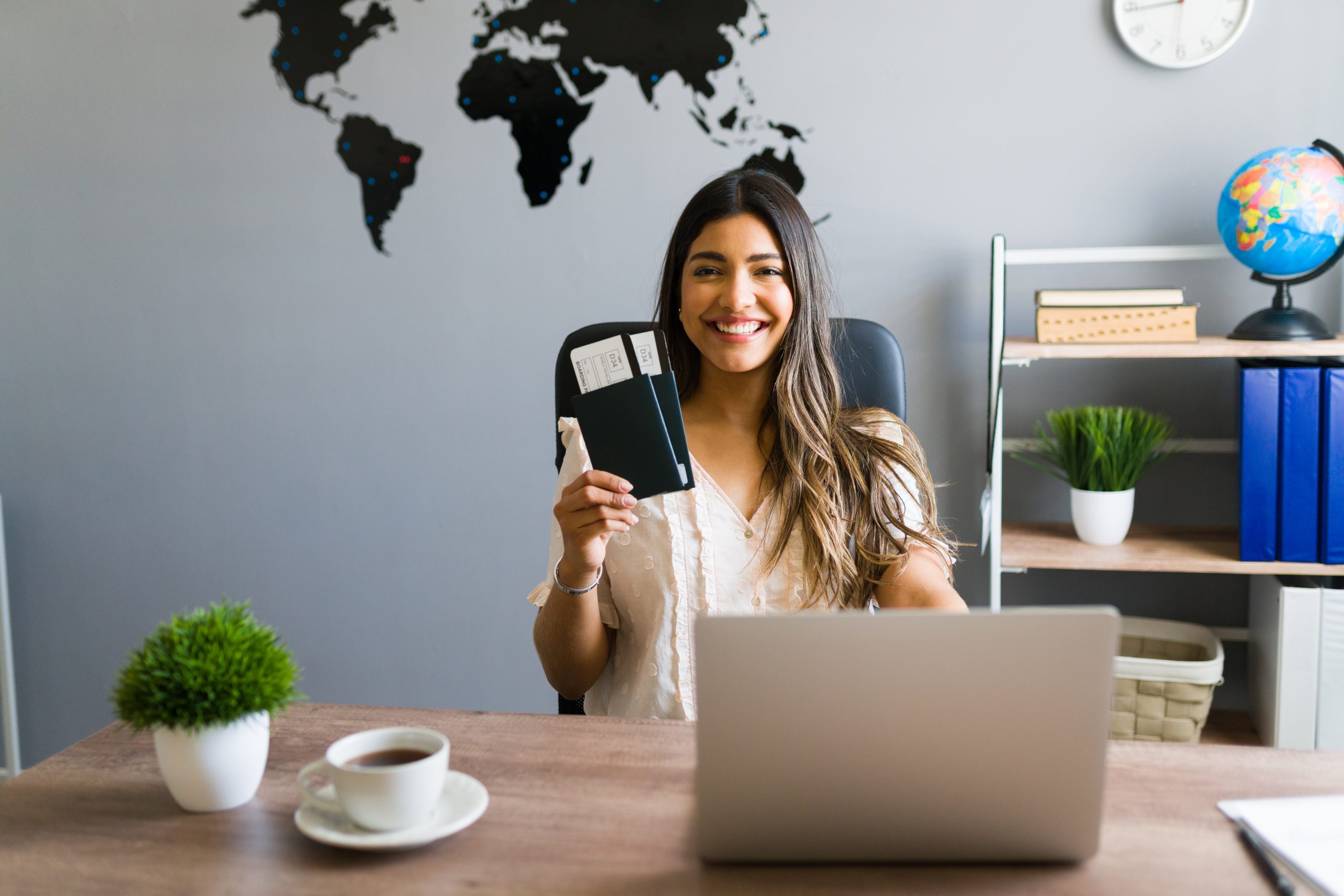 I am here to help you with your booking and travel questions. Female sales agent holding plane tickets while smiling and making eye contact at the travel agency